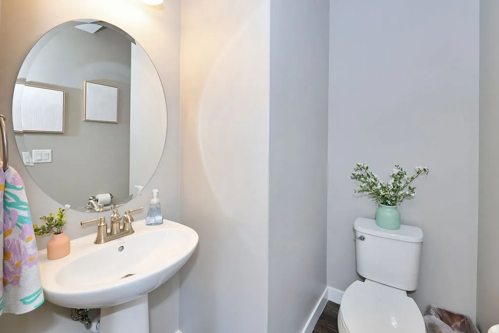 main floor powder Bathroom featuring a pedestal sink, brushed nickel faucet, large circular mirror, and overhead light fixture
