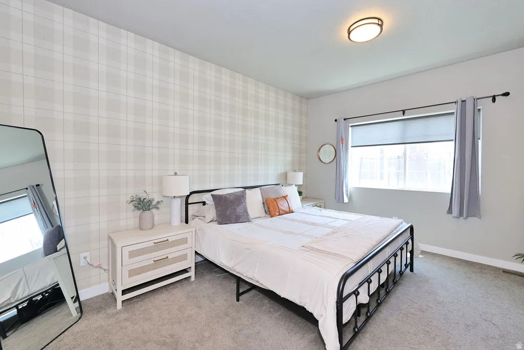 Primary Bedroom featuring a plaid accent wall, a window with roller shade and drapes, and a flush mount ceiling light