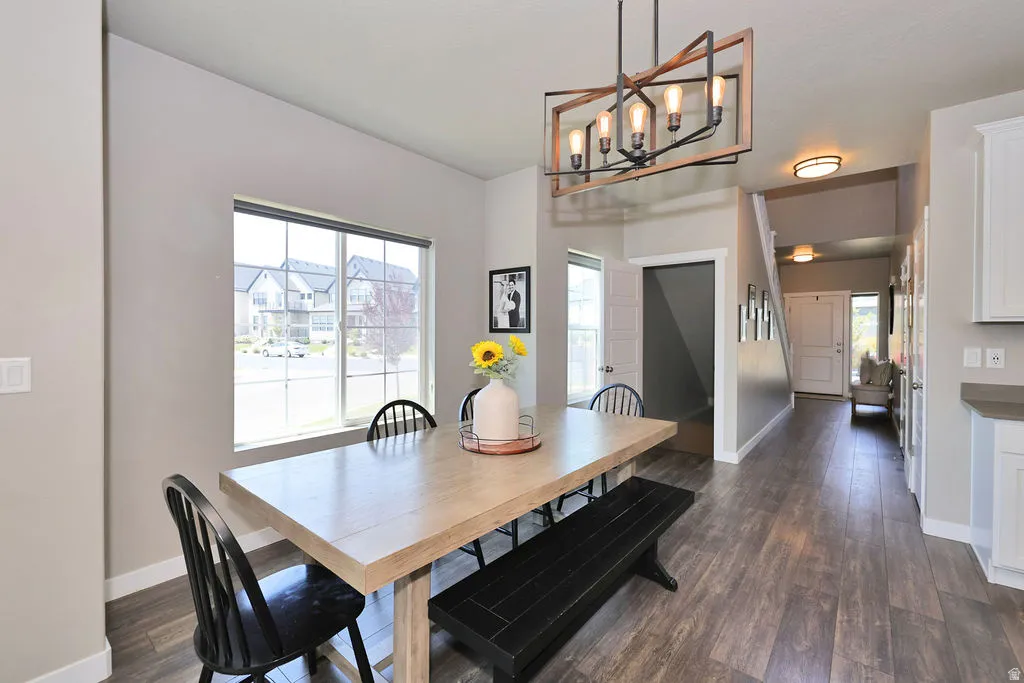 Bright and open dining area featuring a wood-finish dining table with black Windsor-style chairs, hardwood flooring throughout, and abundant natural light from a large picture window