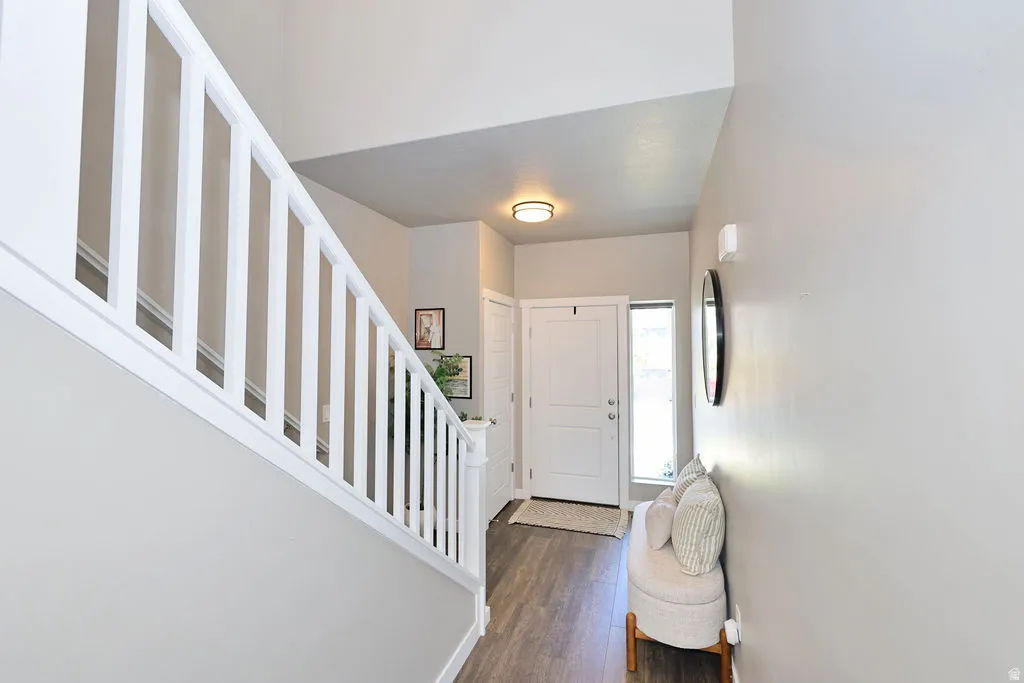 Entryway featuring wood-finish flooring, a white paneled front door, and a staircase with white balusters
