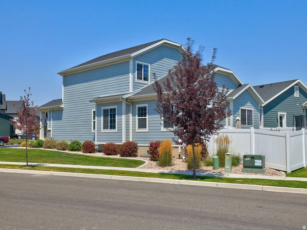 Light blue siding exterior with white trim, featuring a dark shingle roof, white window frames, and a manicured lawn with mature landscaping