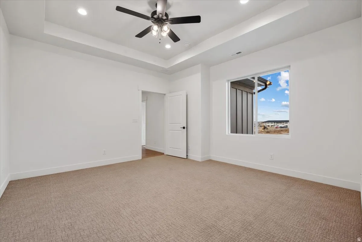 Recessed lighting, ceiling fan, tray ceiling, white walls, and carpeted flooring