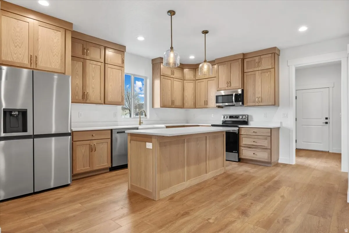Kitchen featuring wood-finish flooring, light wood cabinetry, white countertops, and stainless steel appliances
