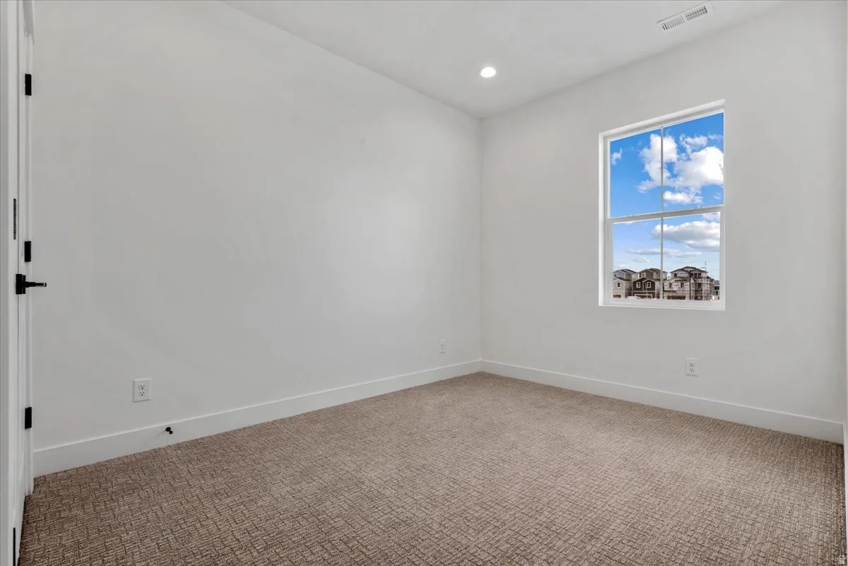 Neutral color palette throughout, featuring a single window, recessed lighting, and patterned carpeting