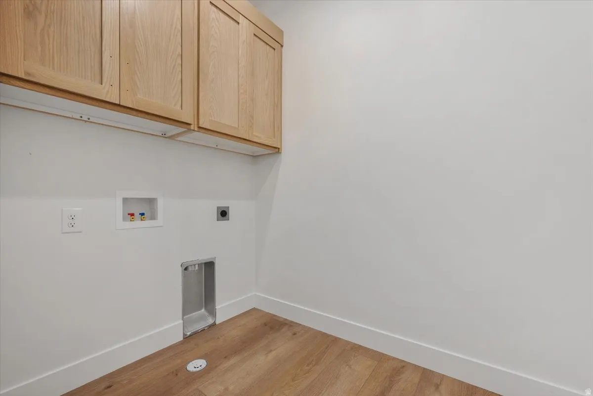 Overhead wood-finish cabinetry, wood-finish flooring, white walls, and built-in laundry hookups