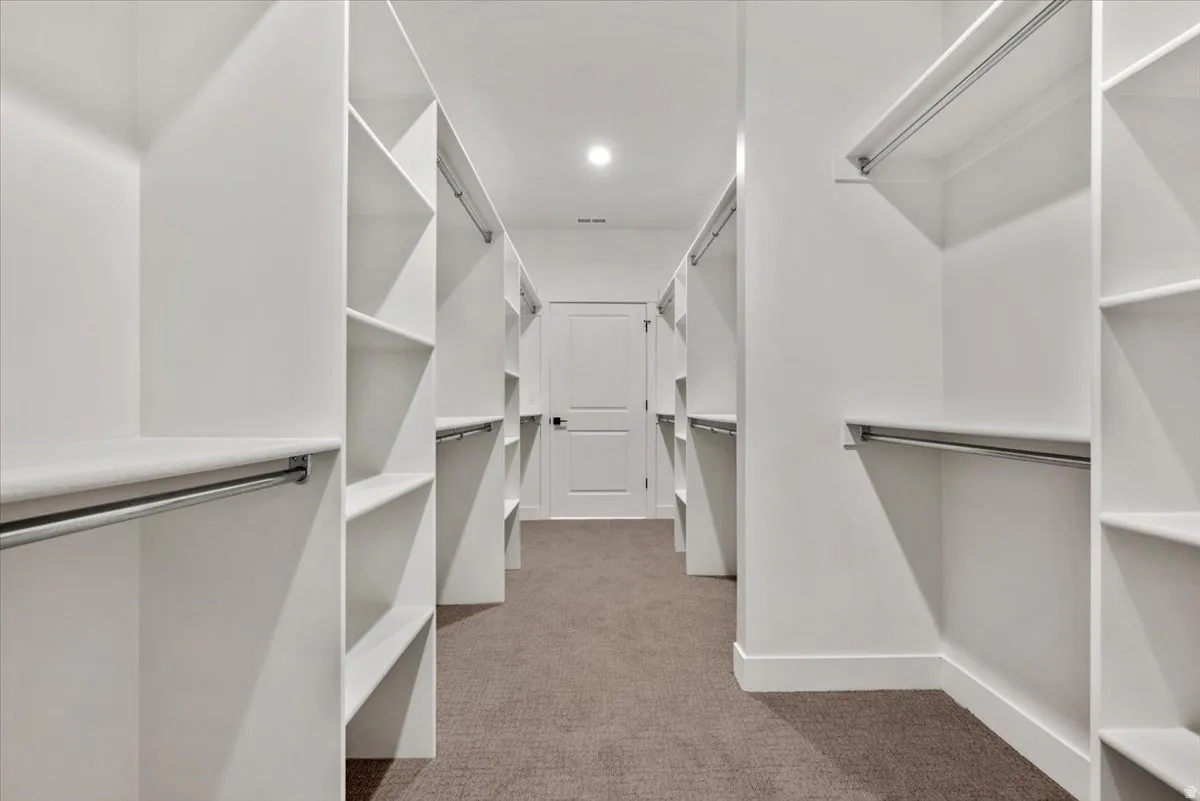 Expansive walk-in closet featuring white built-in shelving, chrome hanging rods, and recessed lighting