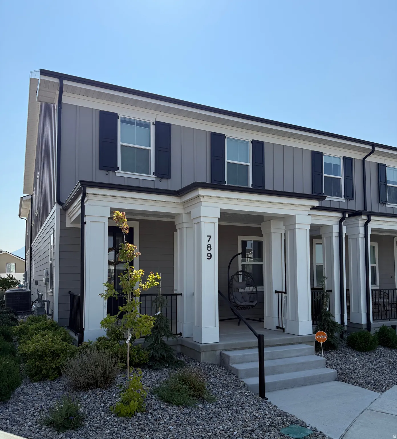 Gray vertical siding facade with black shutters, white columned porch, white trim detailing, and a concrete entryway
