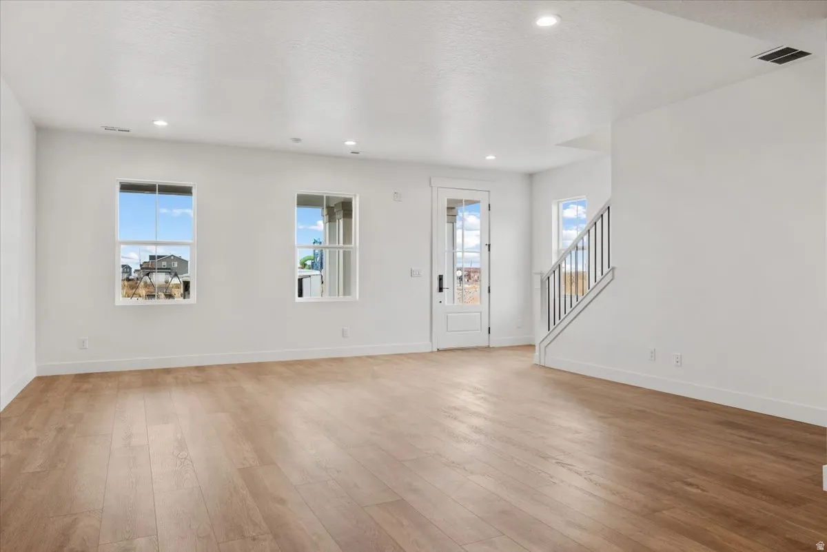 Bright living space featuring recessed lighting, wood-finish flooring, multiple windows, a glass-paneled door, and a staircase with a metal railing