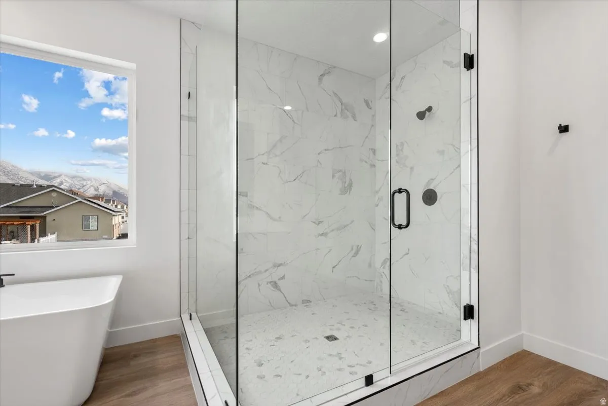 Freestanding soaking tub, glass-enclosed shower with tiled walls and floor, and wood-finish flooring