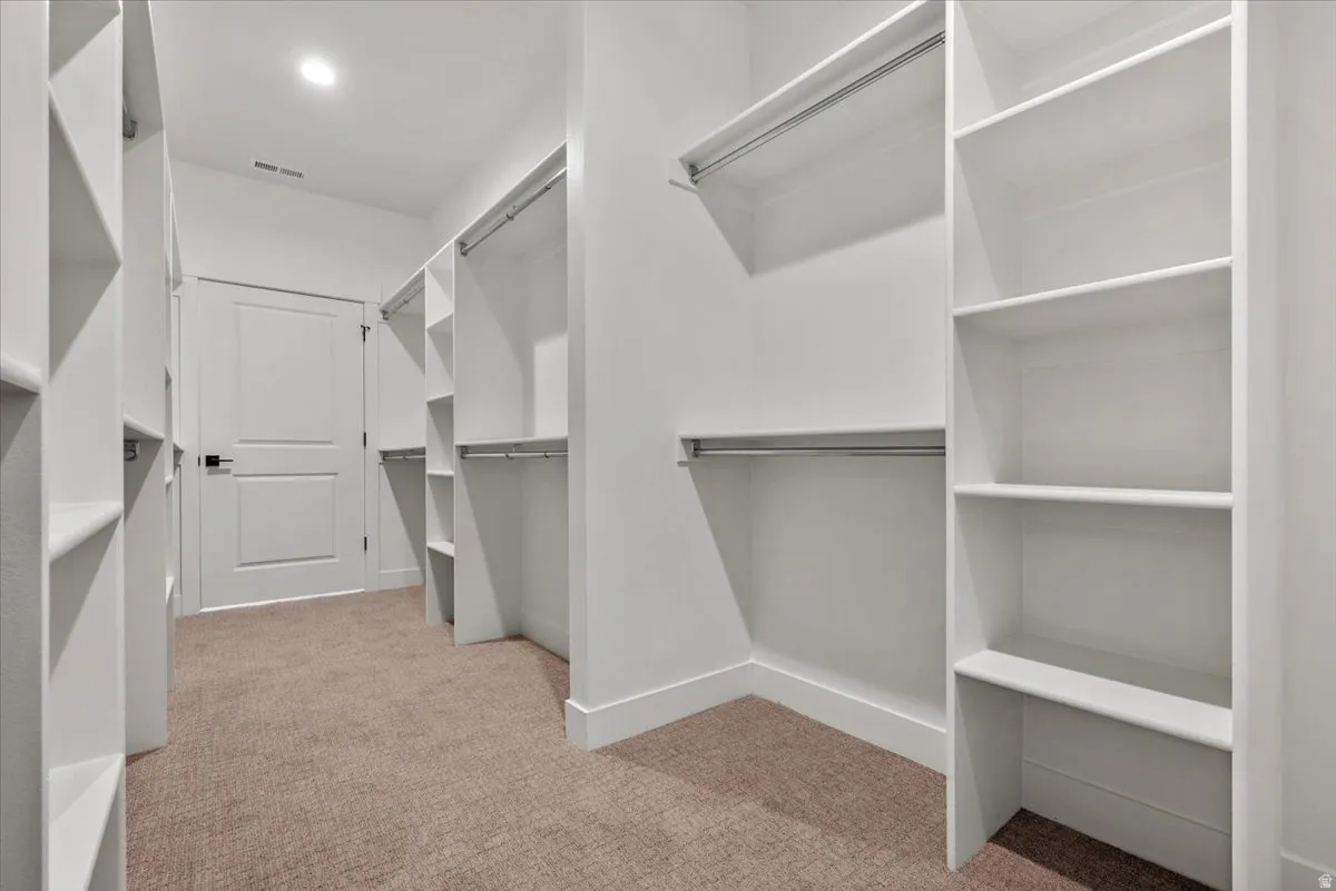 Custom closet system with white shelving, hanging rods, recessed lighting, and carpet flooring
