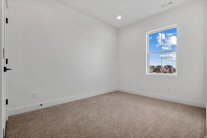 Neutral color palette throughout, featuring a single window, recessed lighting, and patterned carpeting
