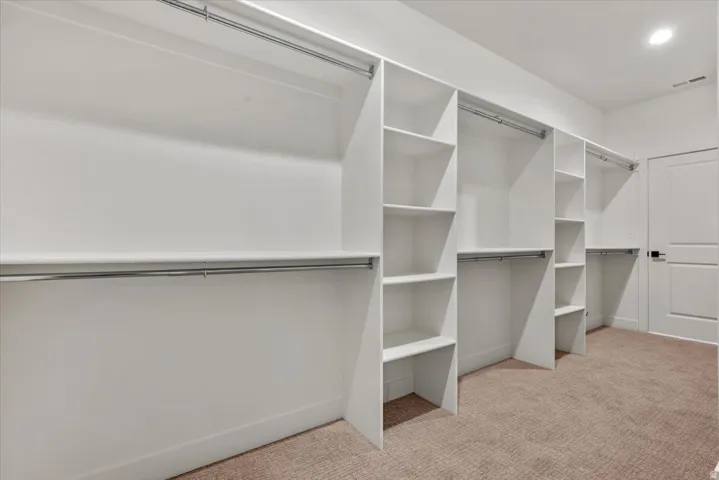 Built-in white shelving and hanging rods, recessed ceiling lighting, and light brown carpet flooring