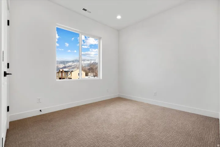 Recessed lighting, white walls, and neutral carpet, with a window showcasing mountain scenery and residential architecture