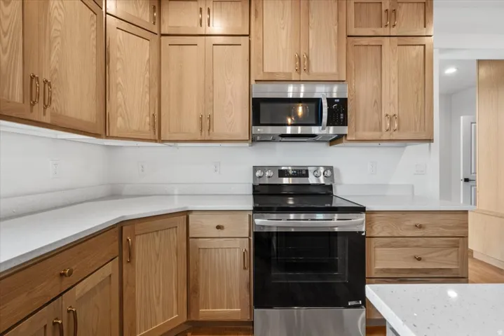 Light wood-finish cabinetry, light-toned countertops, stainless steel microwave, and stainless steel electric range