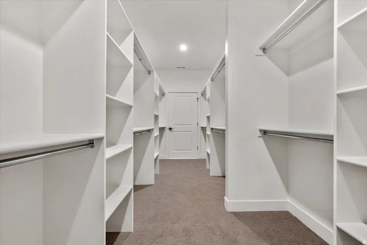 Expansive walk-in closet featuring white built-in shelving, chrome hanging rods, and recessed lighting