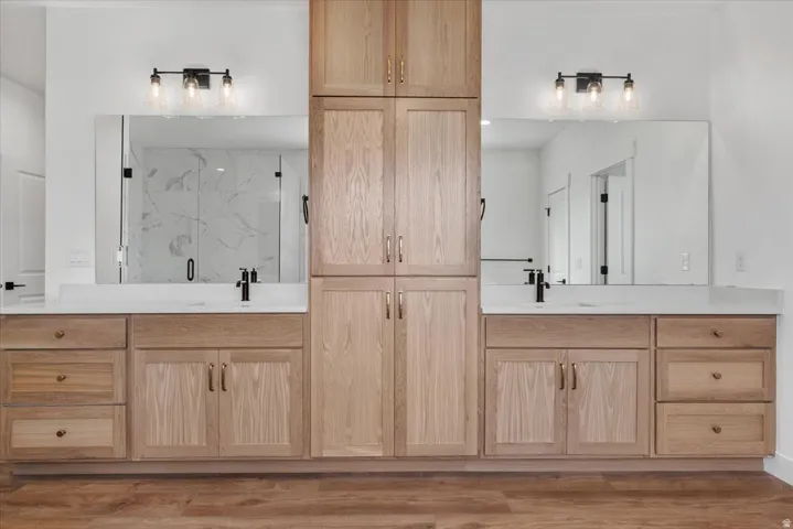 Dual vanities with integrated sinks, light wood-finish cabinetry, and matte black fixtures