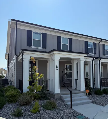 Gray vertical siding facade with black shutters, white columned porch, white trim detailing, and a concrete entryway