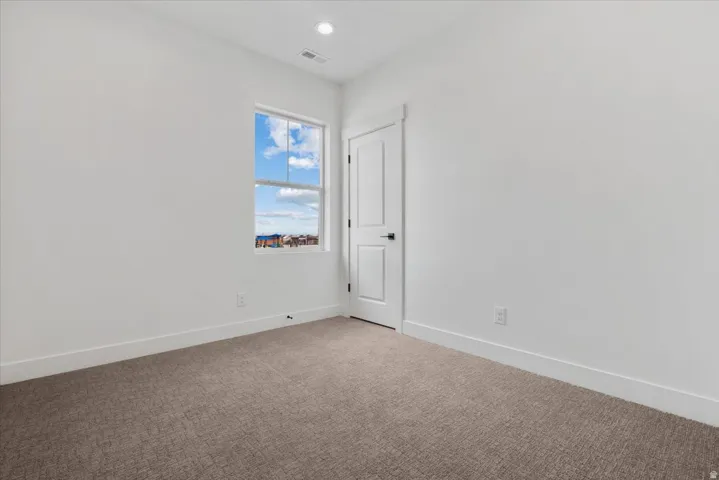 Neutral white wall finishes, single recessed ceiling light, white trim, textured carpet flooring, and a white door with matte black hardware