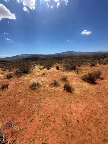 Expansive desert terrain with red earth, sparse low-lying brush, and distant mountain ranges under a clear sky