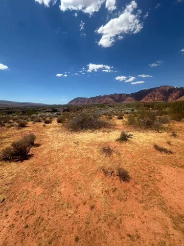 Expansive desert landscape with red earth, sparse low-lying vegetation, and distant red rock mountains