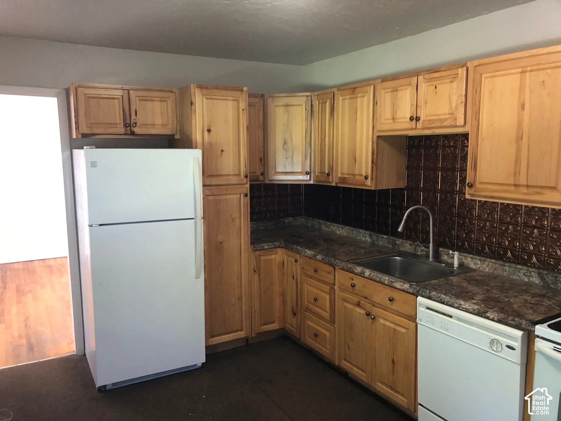 Kitchen featuring wood cabinetry, textured backsplash, laminate countertops, and a stainless steel sink