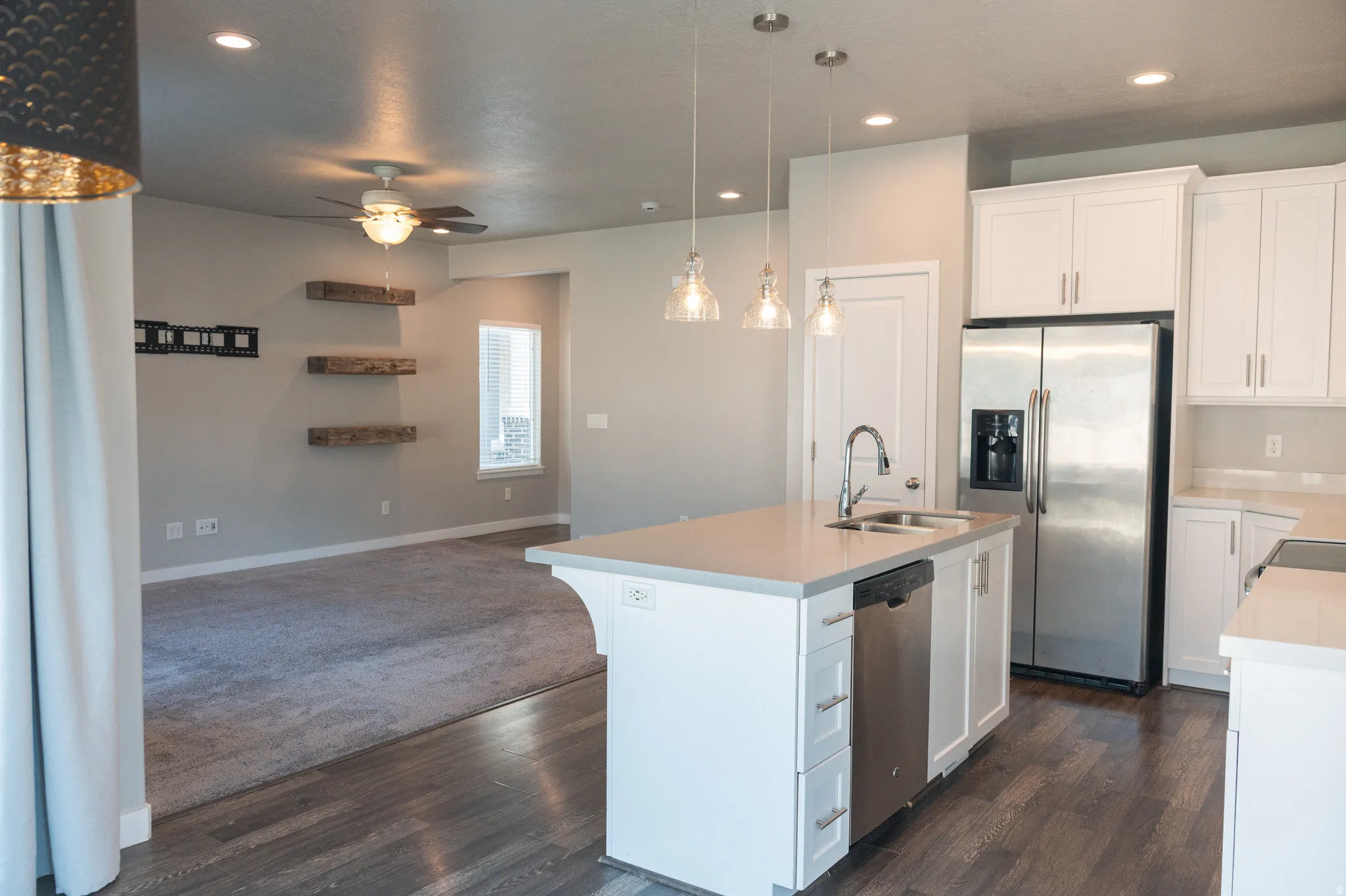 Open-concept living space with a kitchen island, stainless steel appliances, white cabinetry, wood-finish flooring, and recessed lighting