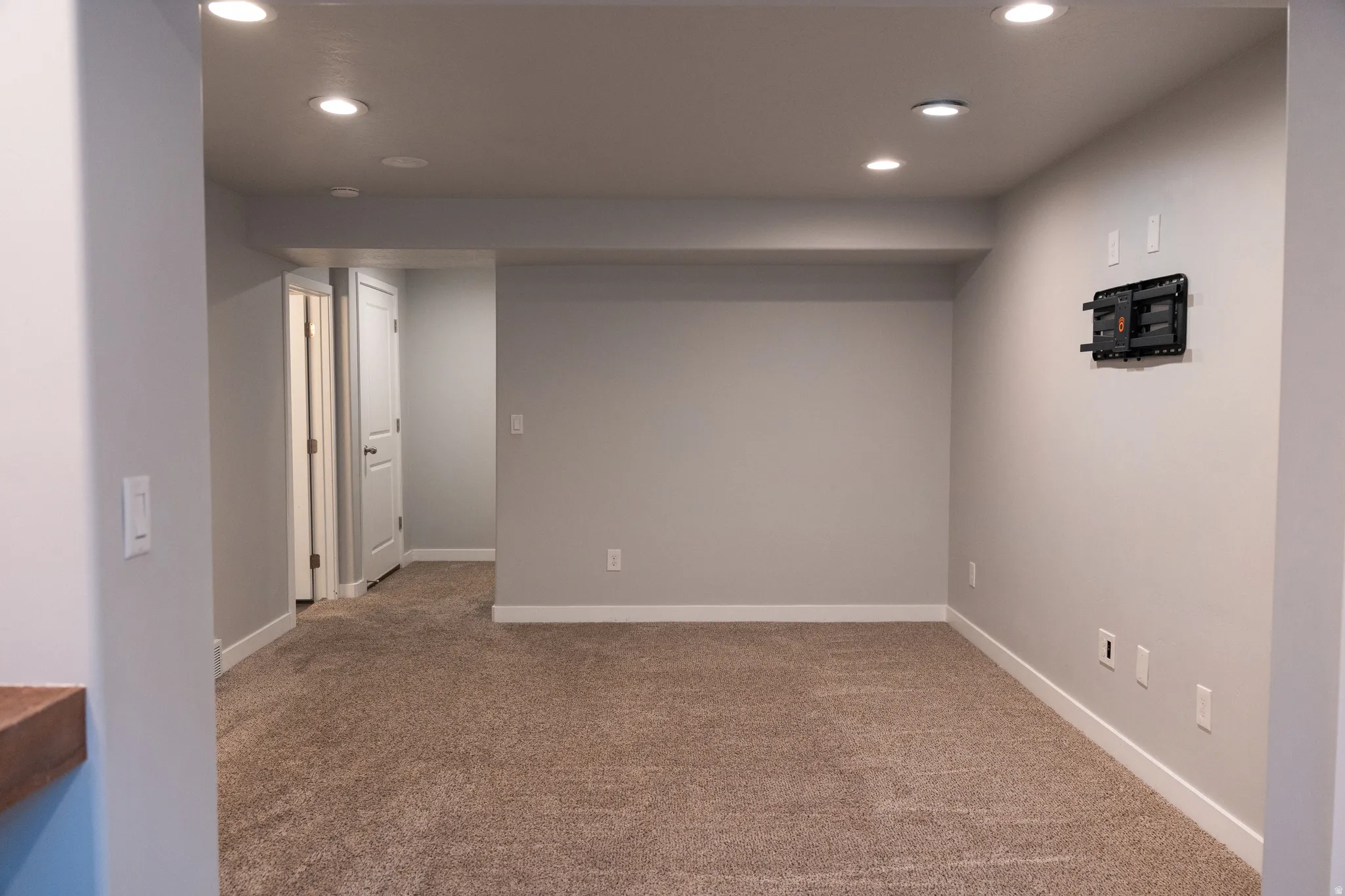 Recessed lighting, light gray wall paint, white trim, and a wall-mounted television bracket