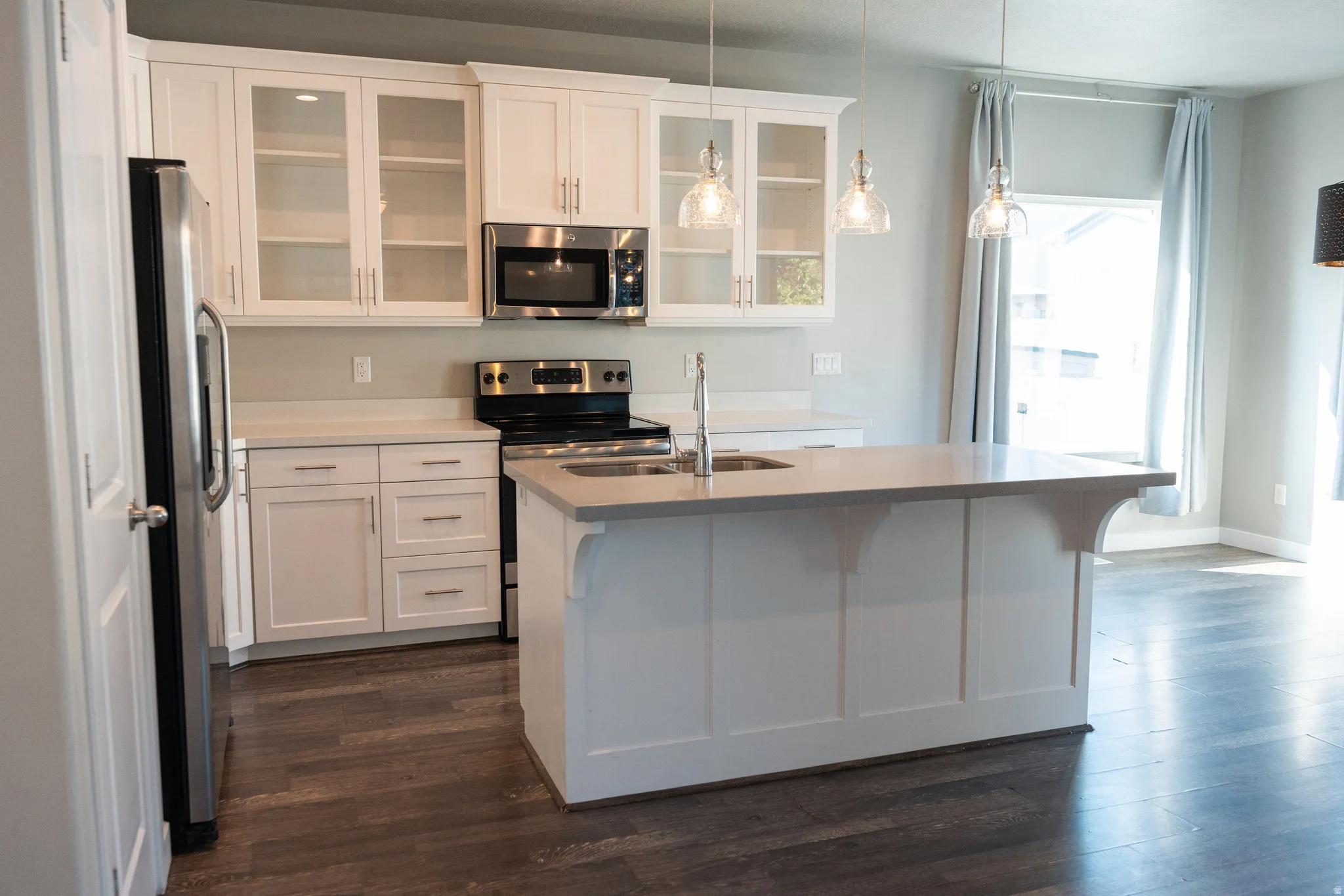 Modern kitchen featuring white cabinetry, stainless steel appliances, a large island with sink, and wood-finish flooring