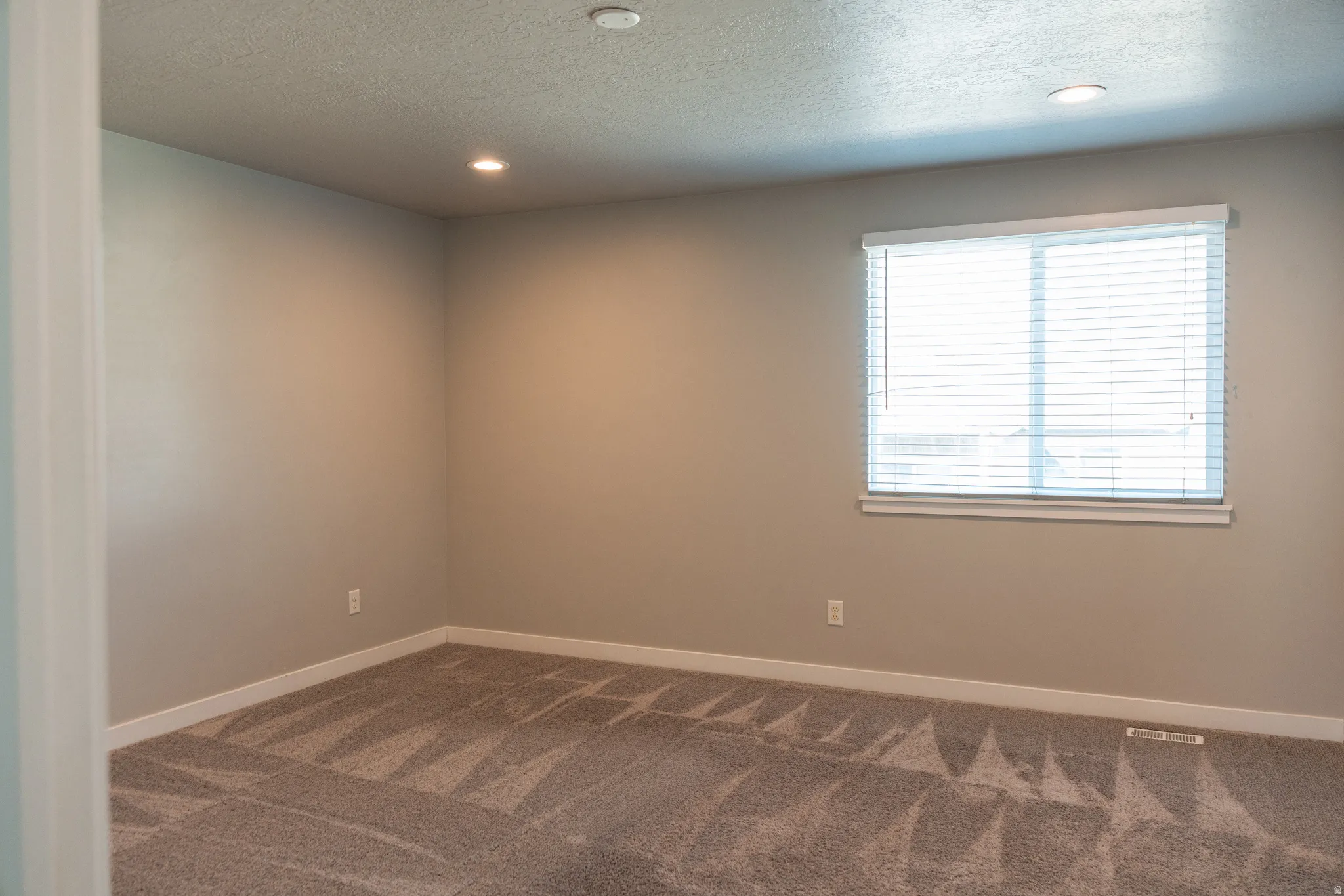 Recessed lighting, neutral wall tones, window with horizontal blinds, carpeted flooring with geometric pattern