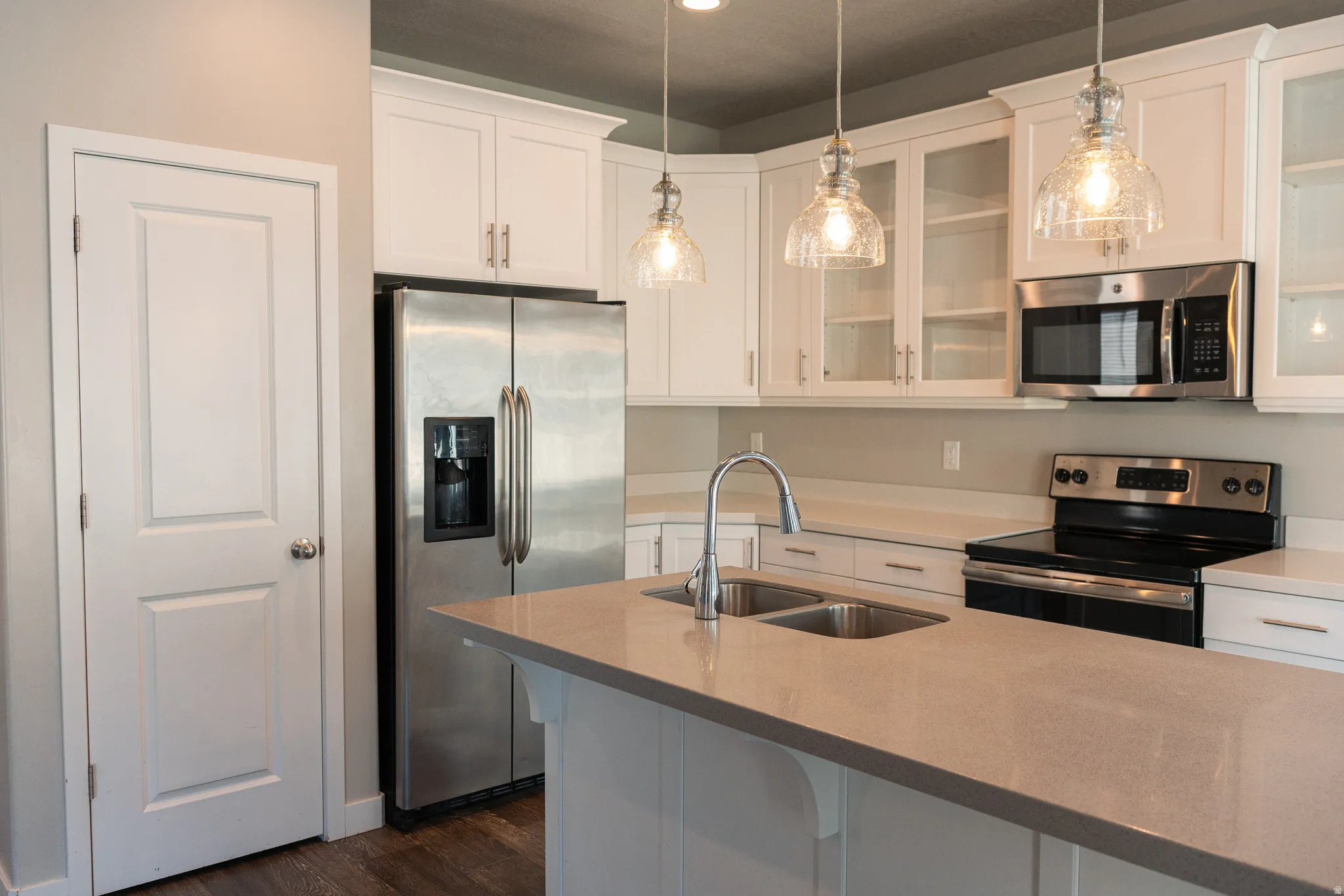Modern kitchen featuring white cabinetry with glass-front upper cabinets, quartz countertops, stainless steel appliances including refrigerator with ice and water dispensers, and a center island with undermount sink