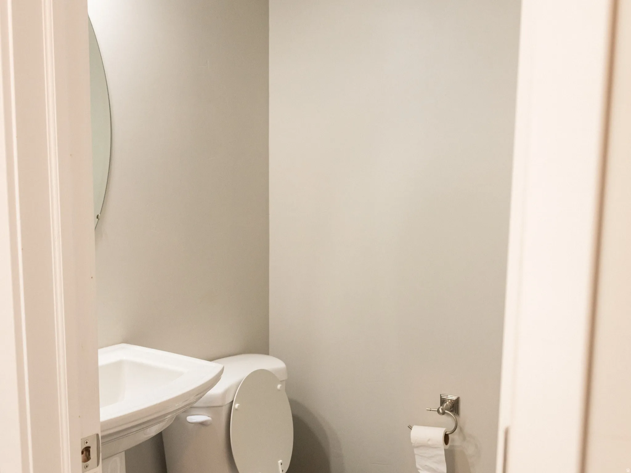 Compact half bath featuring a standard toilet with seat, pedestal sink, chrome wall-mounted faucet, and wood-finish flooring