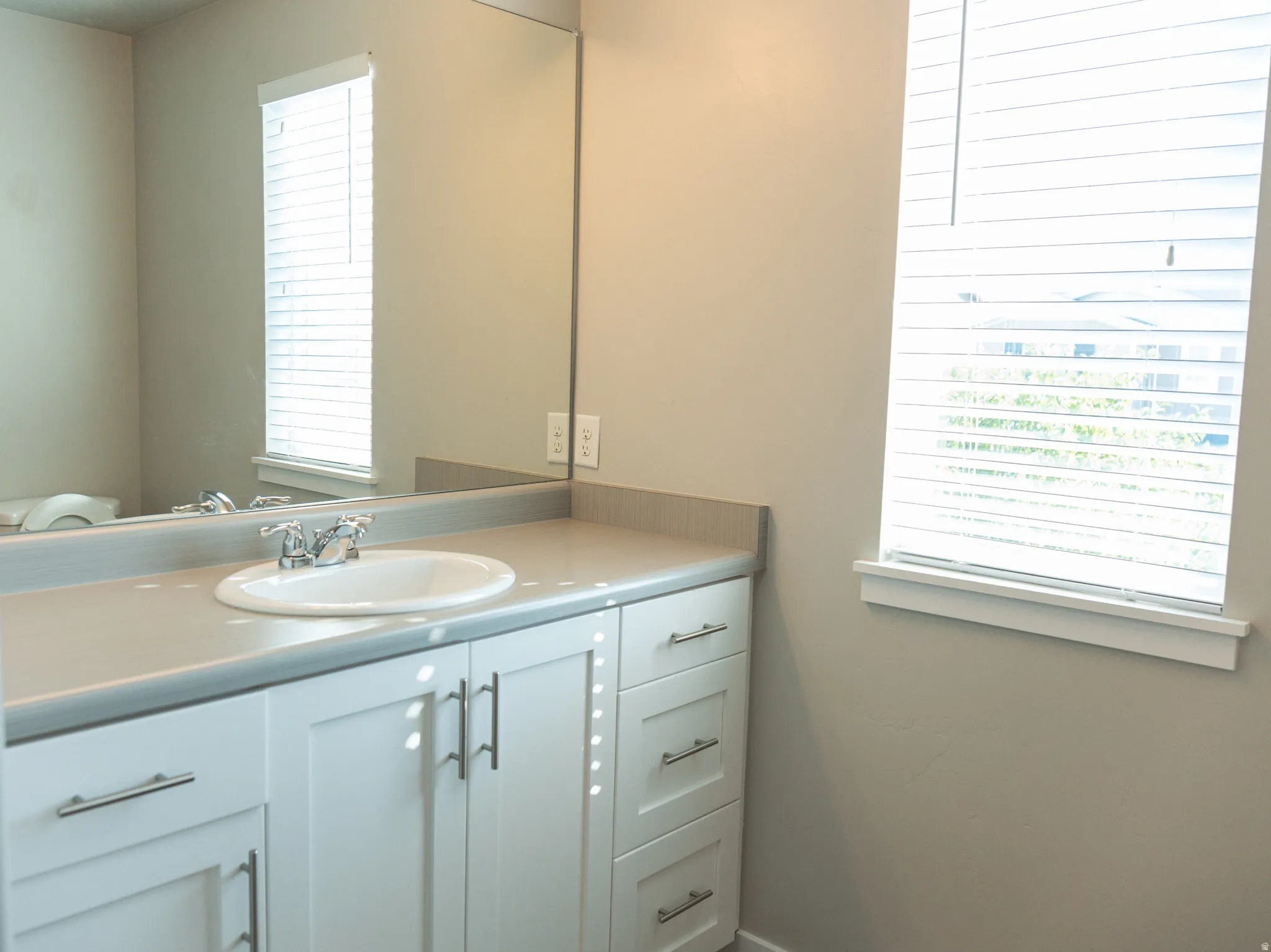 White vanity cabinetry with brushed nickel hardware, solid surface countertop, integrated sink with chrome faucet, and a large wall-mounted mirror
