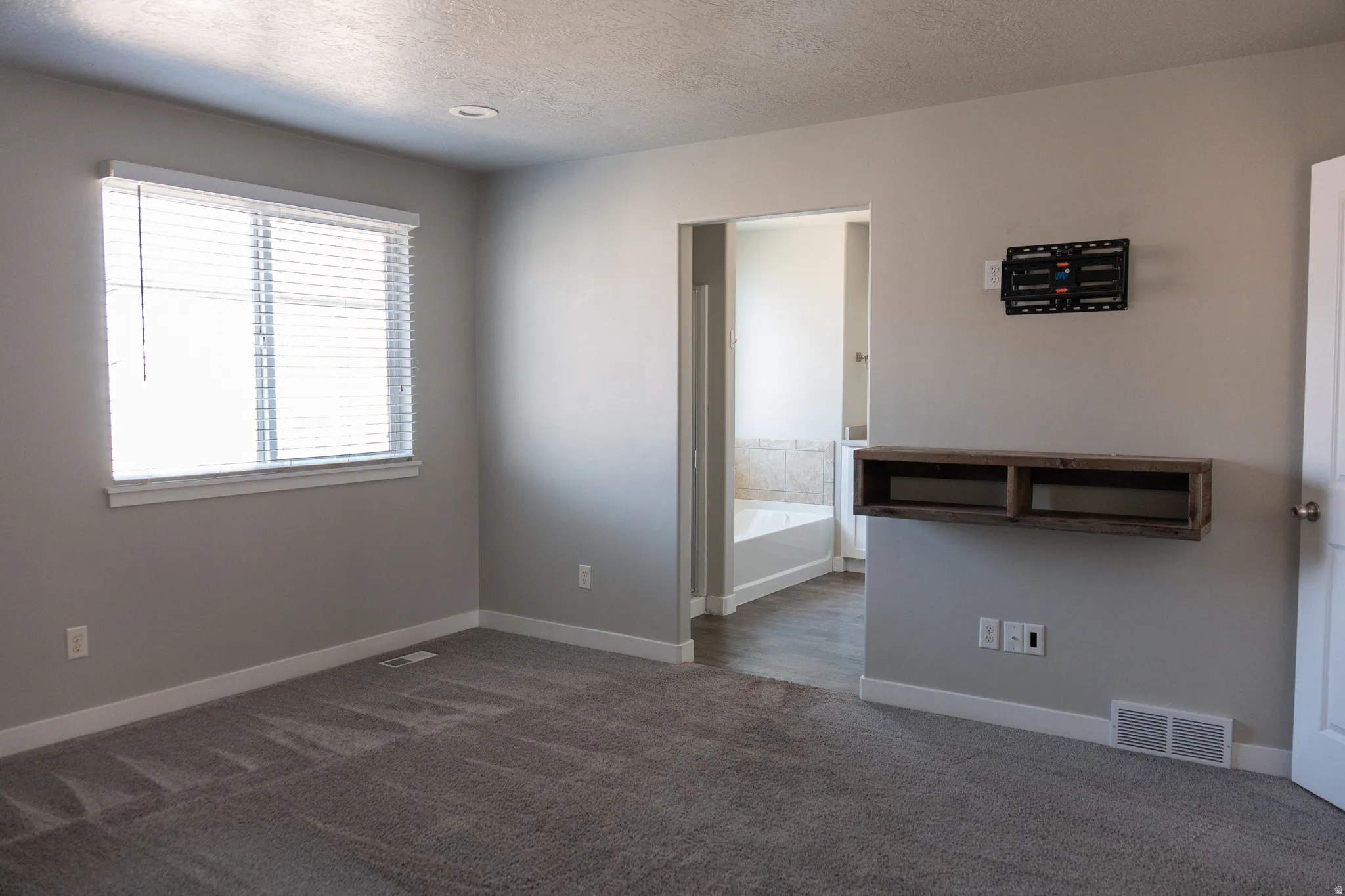 Light gray wall paint, recessed lighting, wall-mounted floating shelf, window with blinds, and gray carpet flooring