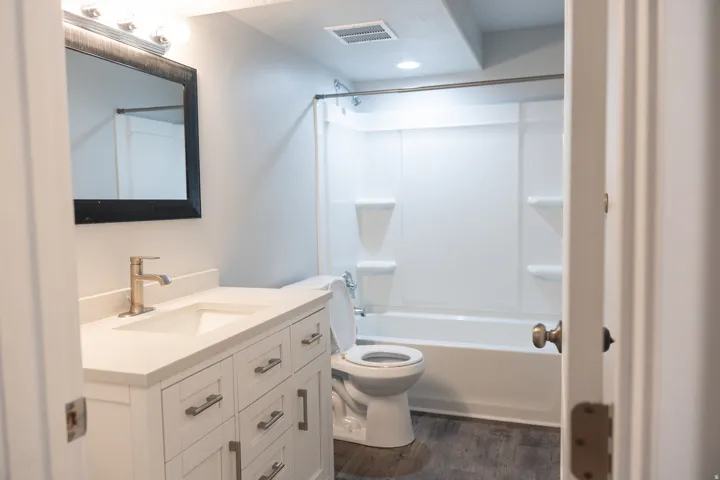Spa-inspired bathroom featuring a custom white vanity with multiple drawers and brushed gold hardware, quartz countertop, vessel sink, and framed mirror with integrated lighting