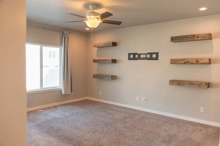 Neutral-toned carpeting, ceiling fan with integrated lighting, recessed lighting, and rustic wood-finish floating shelves