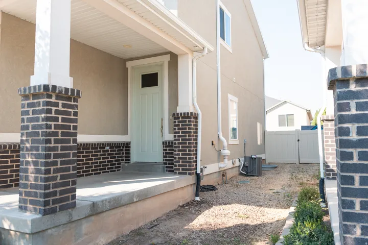Front porch with dark brick columns, concrete steps, and a light-colored entry door