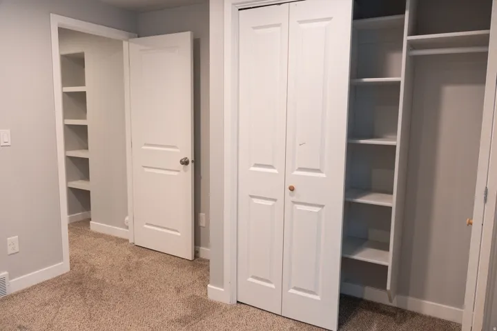 Built-in shelving, carpet flooring, interior doors with hardware, bi-fold closet doors, and a closet rod