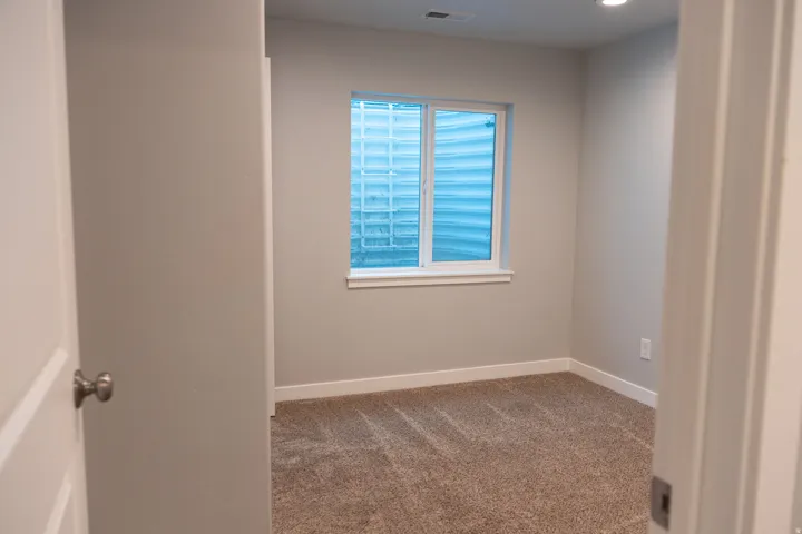 Bright secondary bedroom featuring neutral wall finishes, carpet flooring, a large window with blinds providing natural light, and a closet with a solid-core door