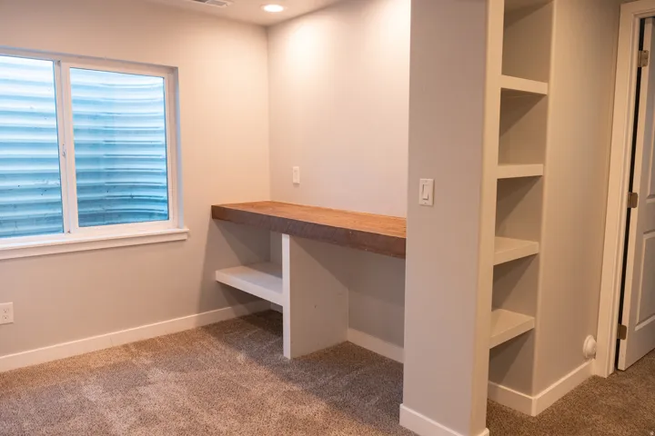 Built-in wood-finish desk with lower shelving, integrated wall shelving, recessed lighting, and carpet flooring