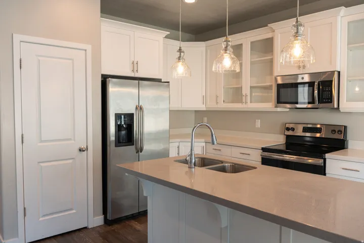 Modern kitchen featuring white cabinetry with glass-front upper cabinets, quartz countertops, stainless steel appliances including refrigerator with ice and water dispensers, and a center island with undermount sink