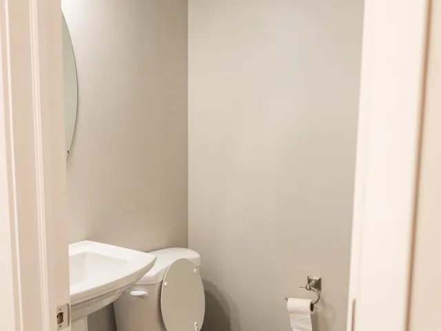 Compact half bath featuring a standard toilet with seat, pedestal sink, chrome wall-mounted faucet, and wood-finish flooring
