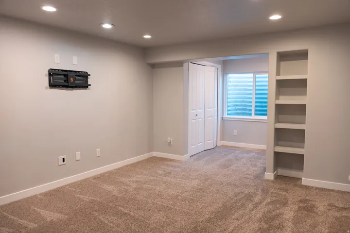 Recessed ceiling lighting, built-in shelving unit, neutral-toned carpeting, white bi-fold closet doors, and a window with horizontal blinds
