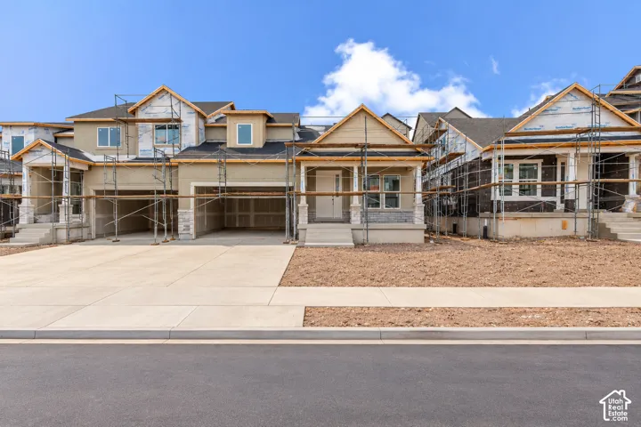 Multi-level exterior featuring stone veneer accents, covered front porch, composite shingle roof, and attached multi-car garage with concrete driveway