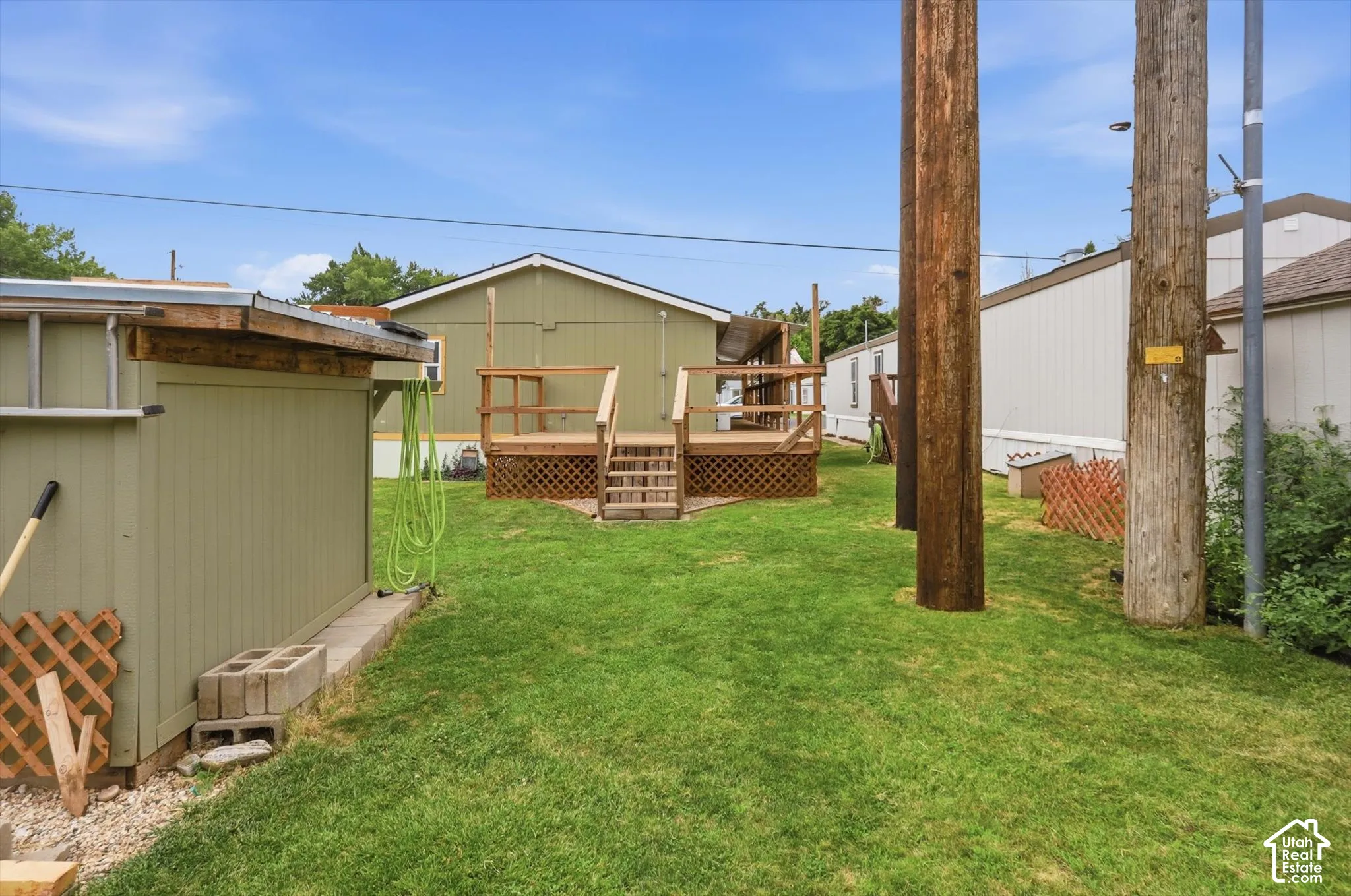 Expansive grassy yard featuring a wooden deck with railing and stairs, and an exterior storage shed
