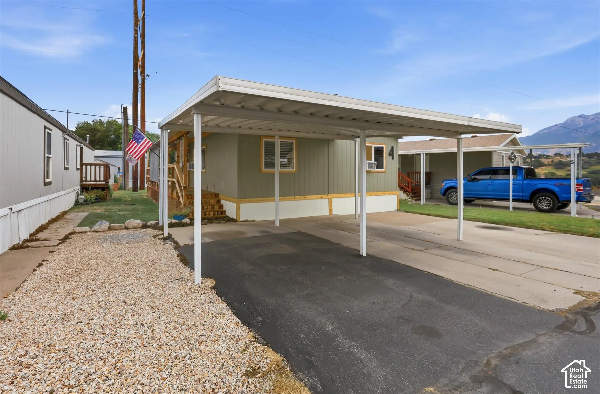 Carport with paved driveway, gravel landscaping, and wooden exterior stairs
