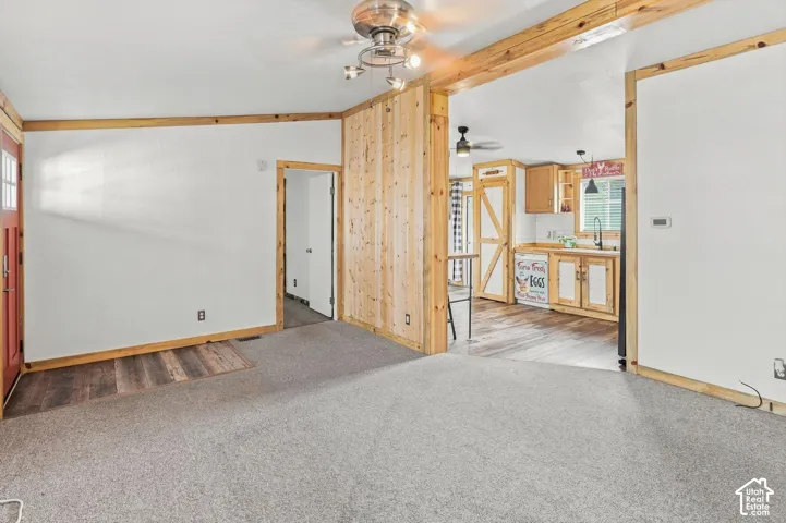 Carpeted flooring, wood-finish accent wall, wood-finish trim, wood-finish flooring, and a ceiling fan with integrated lighting