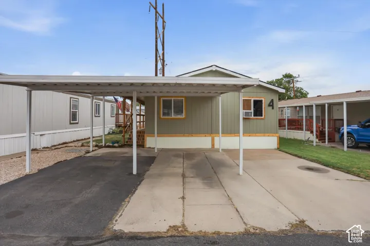 Gabled roofline, light green siding, covered carport, concrete driveway, and gravel landscaping