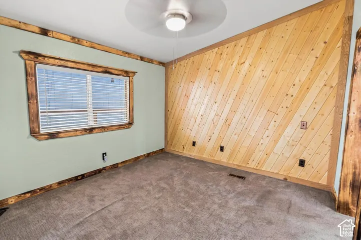 Plank wood accent wall, wood-trimmed window, wood-finish trim, ceiling fan light fixture, and carpeted flooring