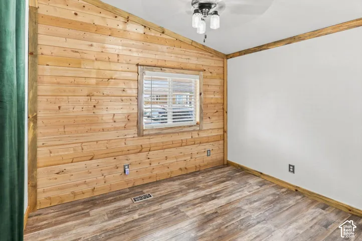 Wood-finish flooring, accent wood paneling, ceiling fan with light fixture, and window with blinds