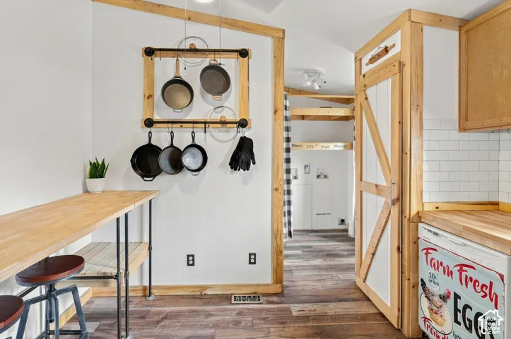 Wood-finish flooring, white subway tile backsplash, light wood cabinetry, and a wood-top counter